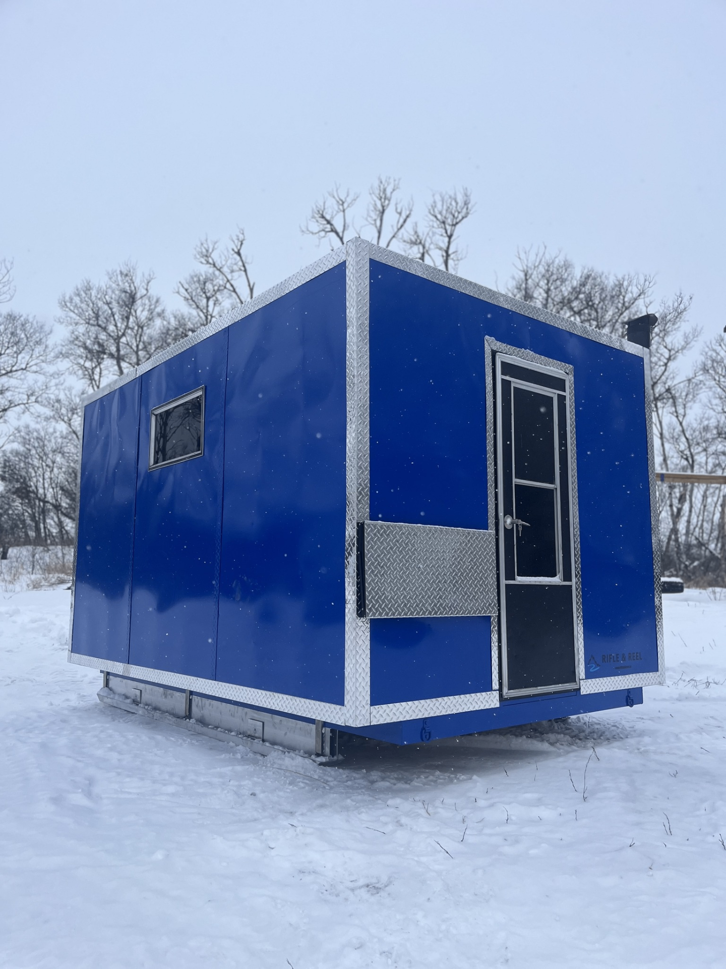 Blue welded aluminum ice shack with diamond-plate trim on snow
